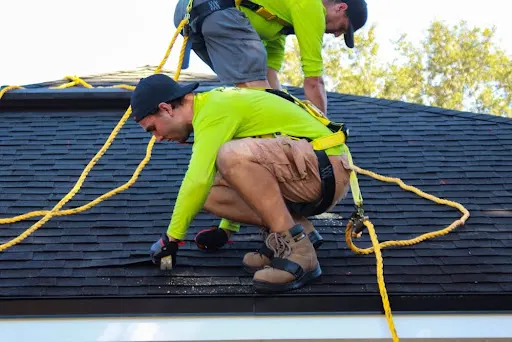 Two roofers wearing safety harnesses working on a shingled roof