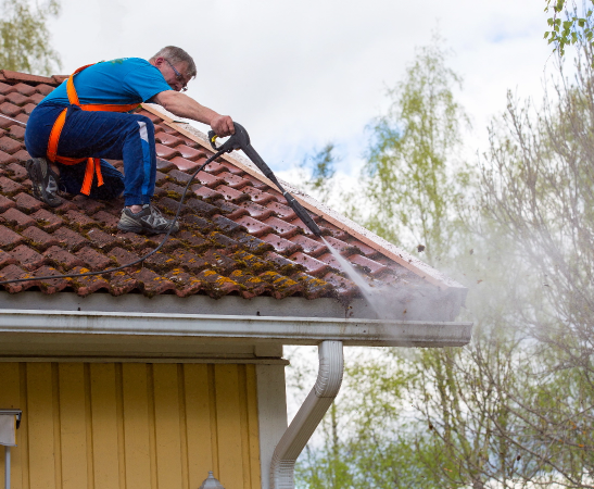 A roofer with a power washer cleaning a roof.