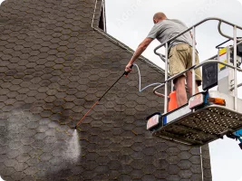 A roofer power washing a roof.