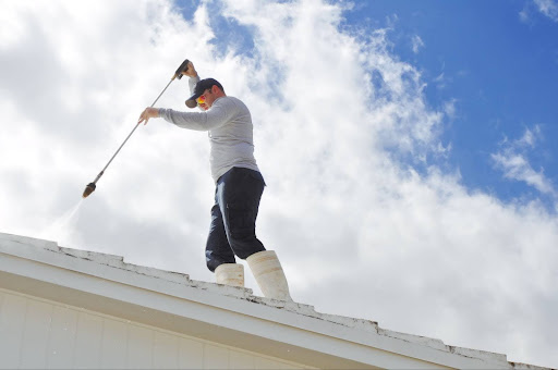 A roofer power-washing a roof.